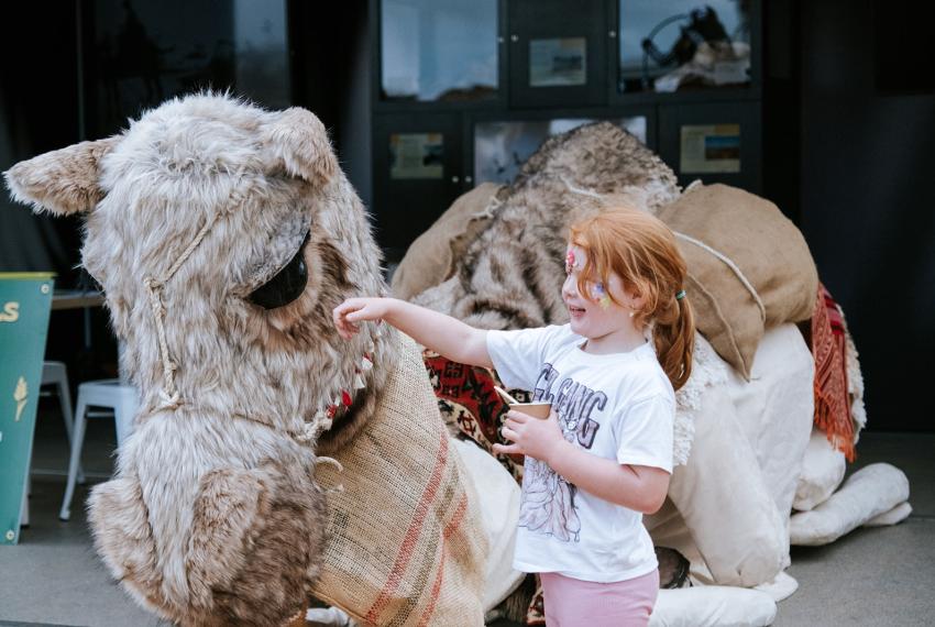Young girl with red hair pats a giant camel puppet