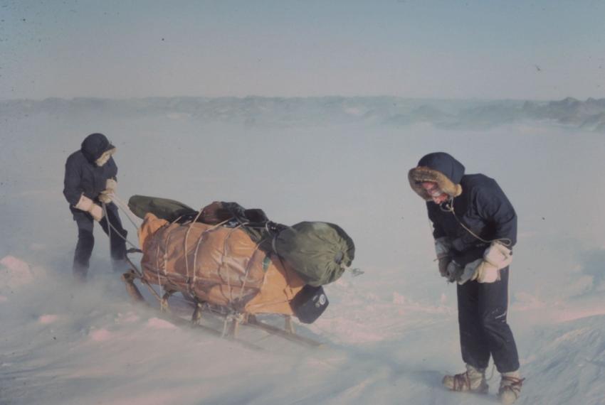 Two people dragging a heavy sled through thick snow and ice.