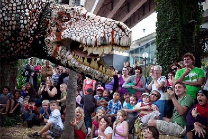 A massive dinosaur puppet meeting a crowd of children