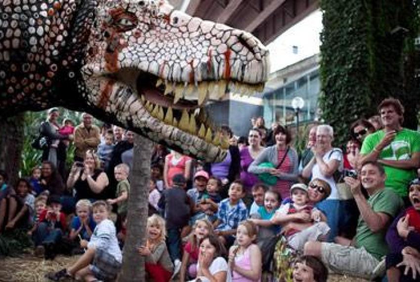 A massive dinosaur puppet meeting a crowd of children