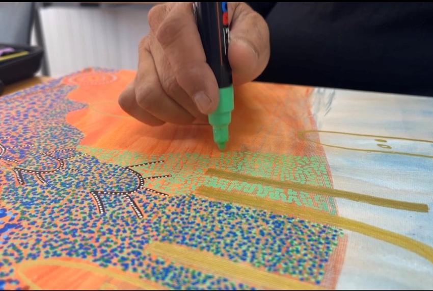 a close up of a colourful artwork and the artists hand adding to the work