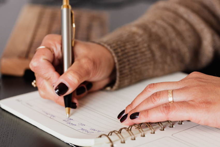 Close up of a pair of hands with black nailpolish writing in a notebook