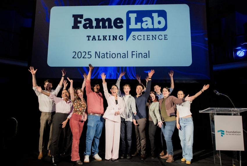 A group of people celebrating on stage, with a large screen displaying the word FameLab behind them.