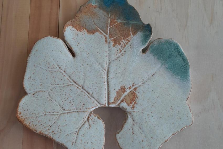 a close up of a ceramic leaf painted in greens and browns