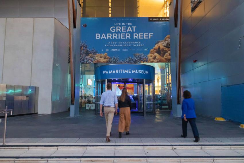 Three people walking to the entrance of the WA Maritime Museum, displaying advertising for Life in the Great Barrier Reef