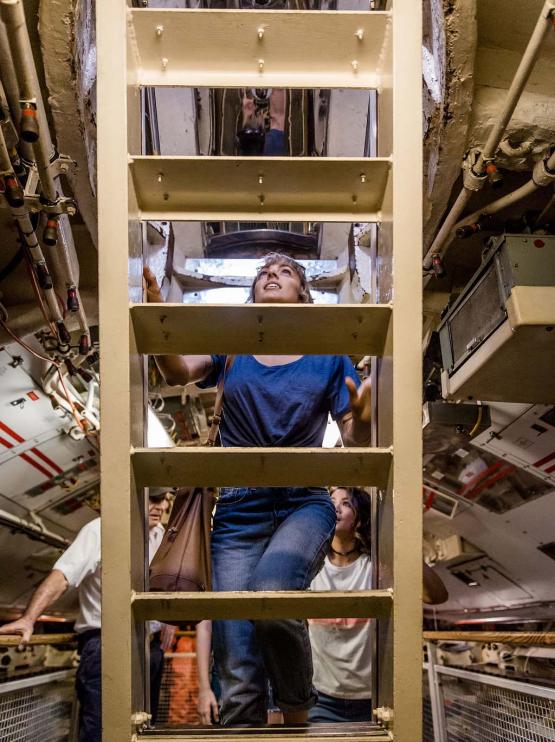 A participant on the immersive tour of the HMAS Ovens climbs a ladder