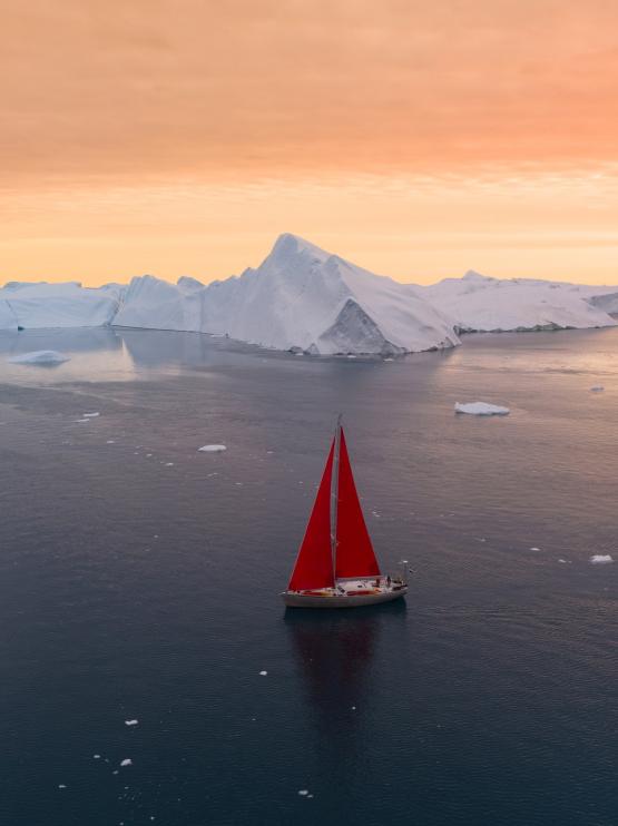 boat with red sails is sailing in water with icebergs in the background