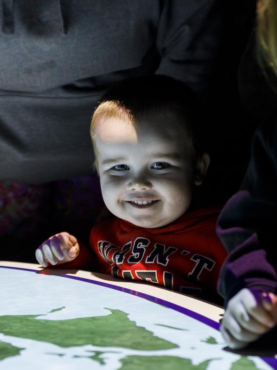 Young child smiling at camera behind a projection of the world map on a table