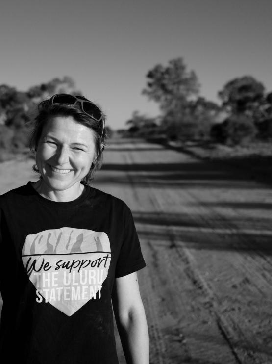 A woman standing on a dirt road, smiling at the camera