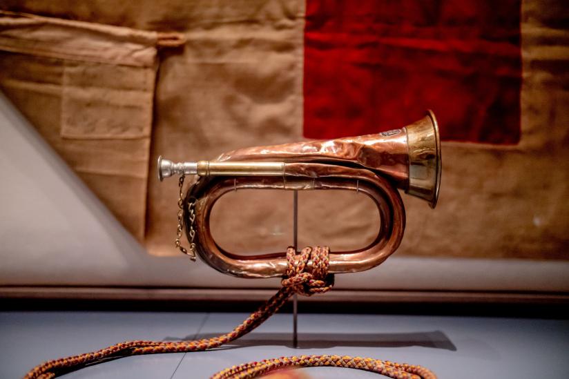 A bronze bugle points right, propped in front of a brown and red piece of material