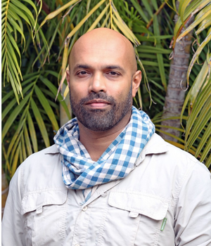 Man in jungle setting and green scarf around his neck.