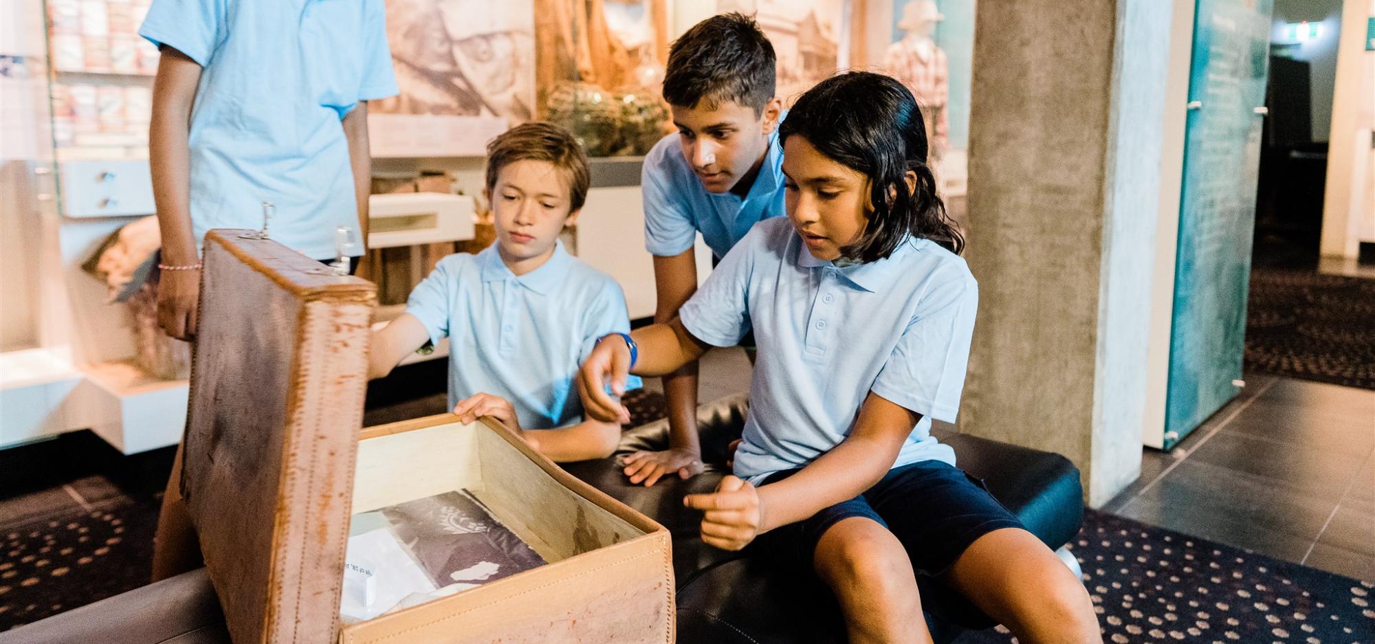 Seated children in school uniform look inside an old-fashioned suitcase