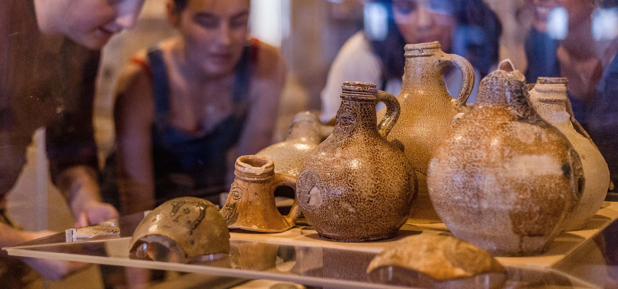 Four people examine a museum showcase filled with ceramic objects