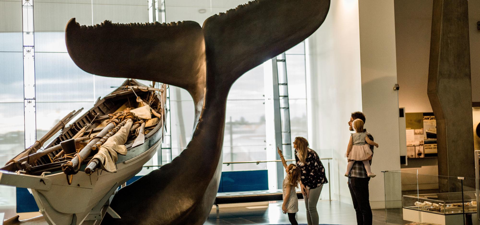 A family pause to examine a large model of a whale's tail in a museum