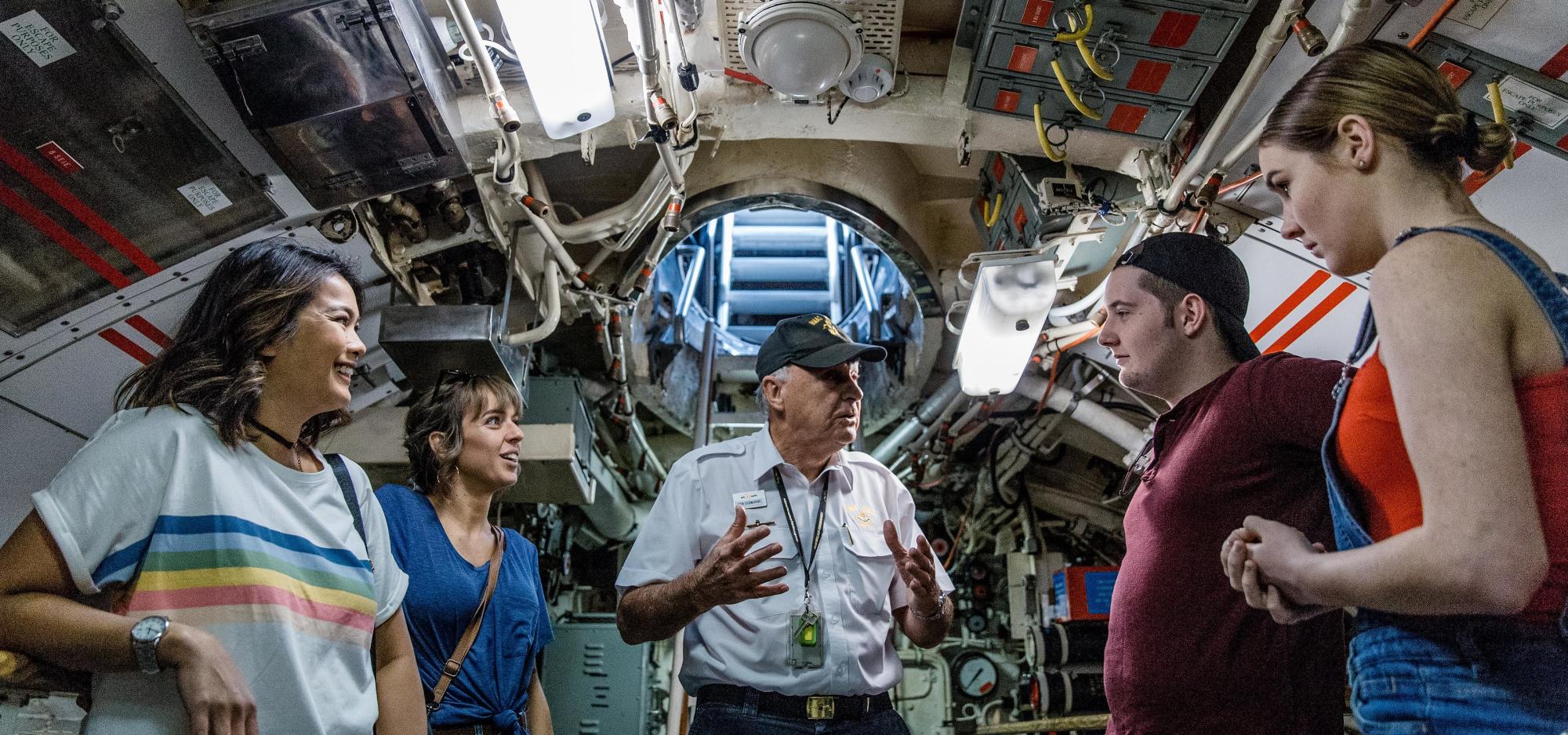 A tour group stand inside the HMAS Ovens, listening to their tour guide