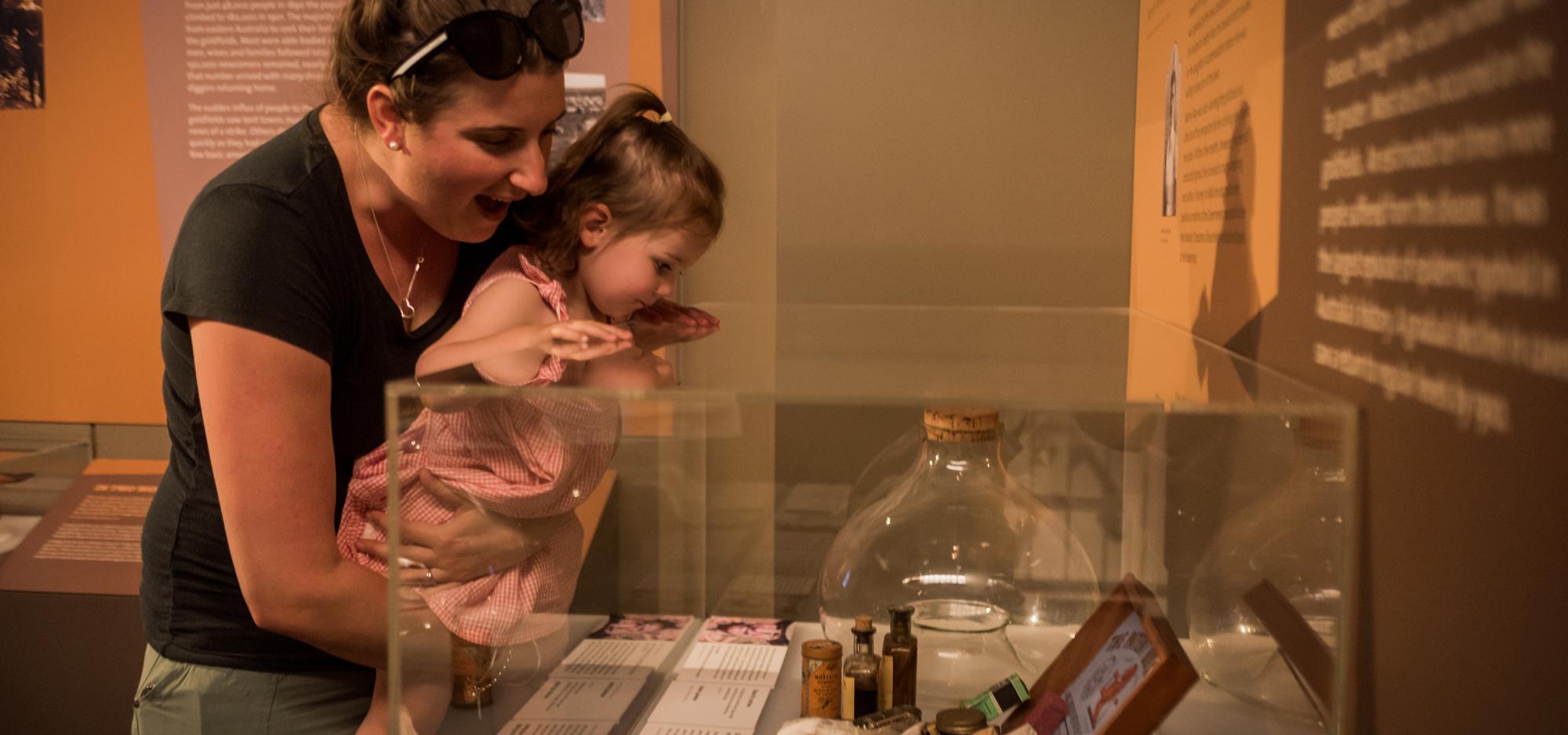 A woman holding a young child looks into a museum showcase