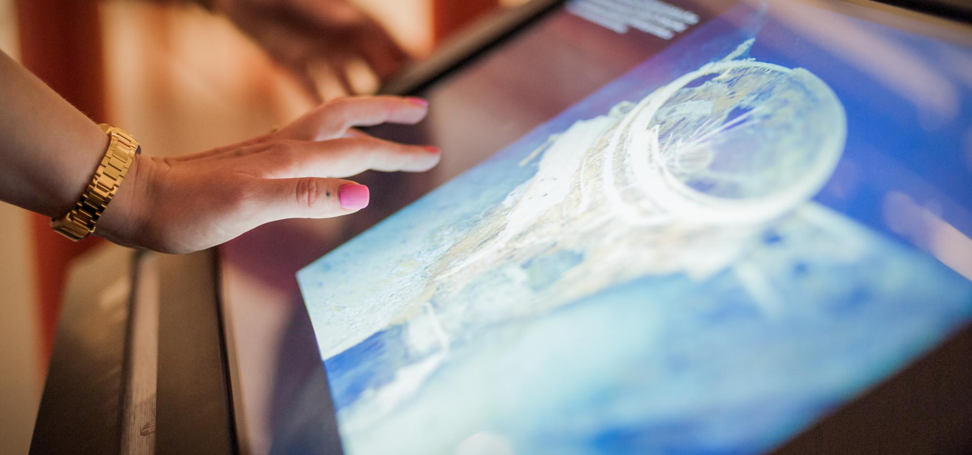 A close up view of a person's hands as they interact with a digital exhibit at Museum of the Goldfields
