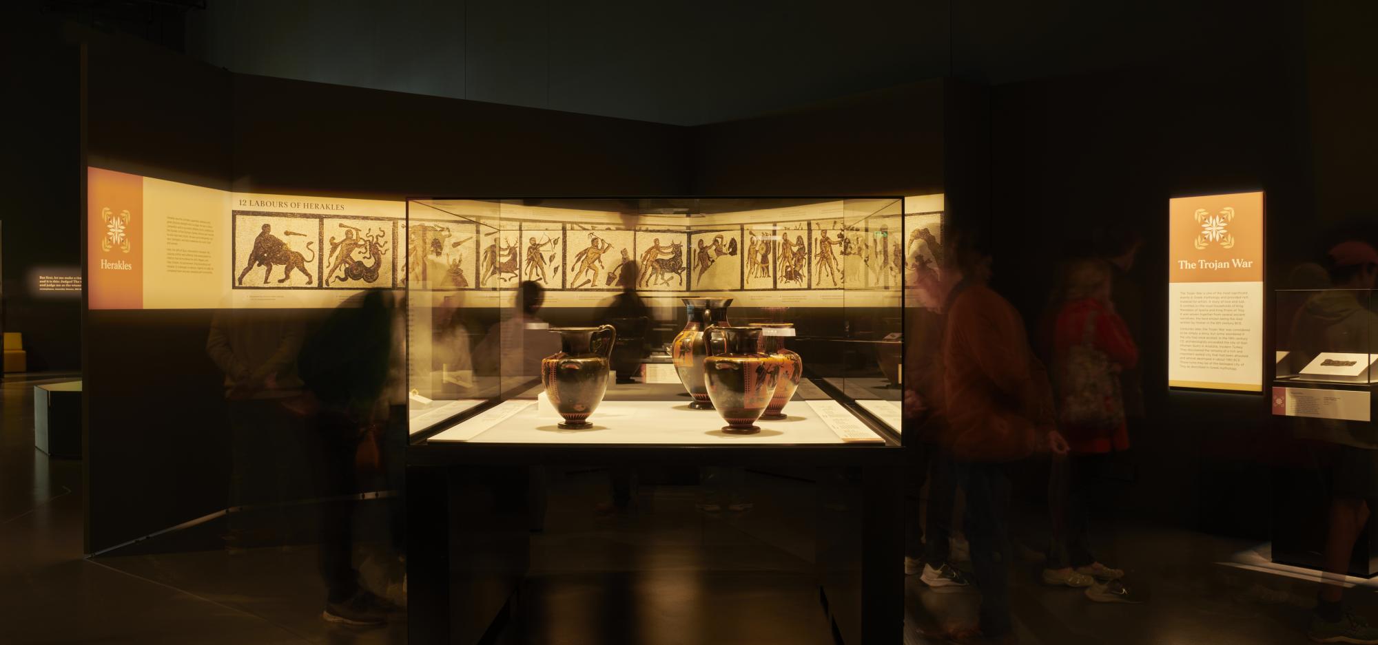 Visitors examine a set of Ancient Greek amphorae in a museum showcase