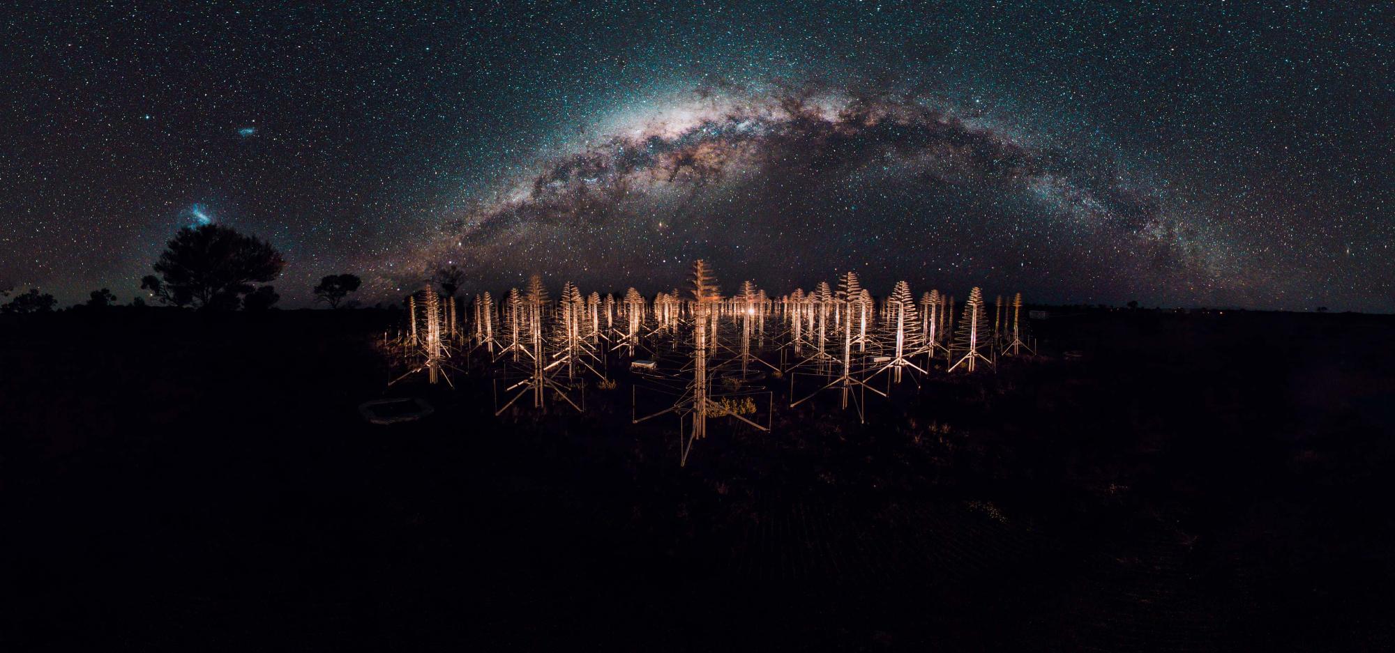 A field of radio telescope antennae under a starry night sky