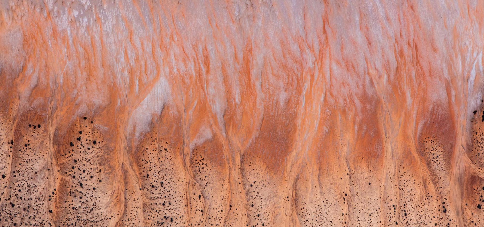 An aerial view of a hilly striated salt lake landscape in shades of red, yellow and white