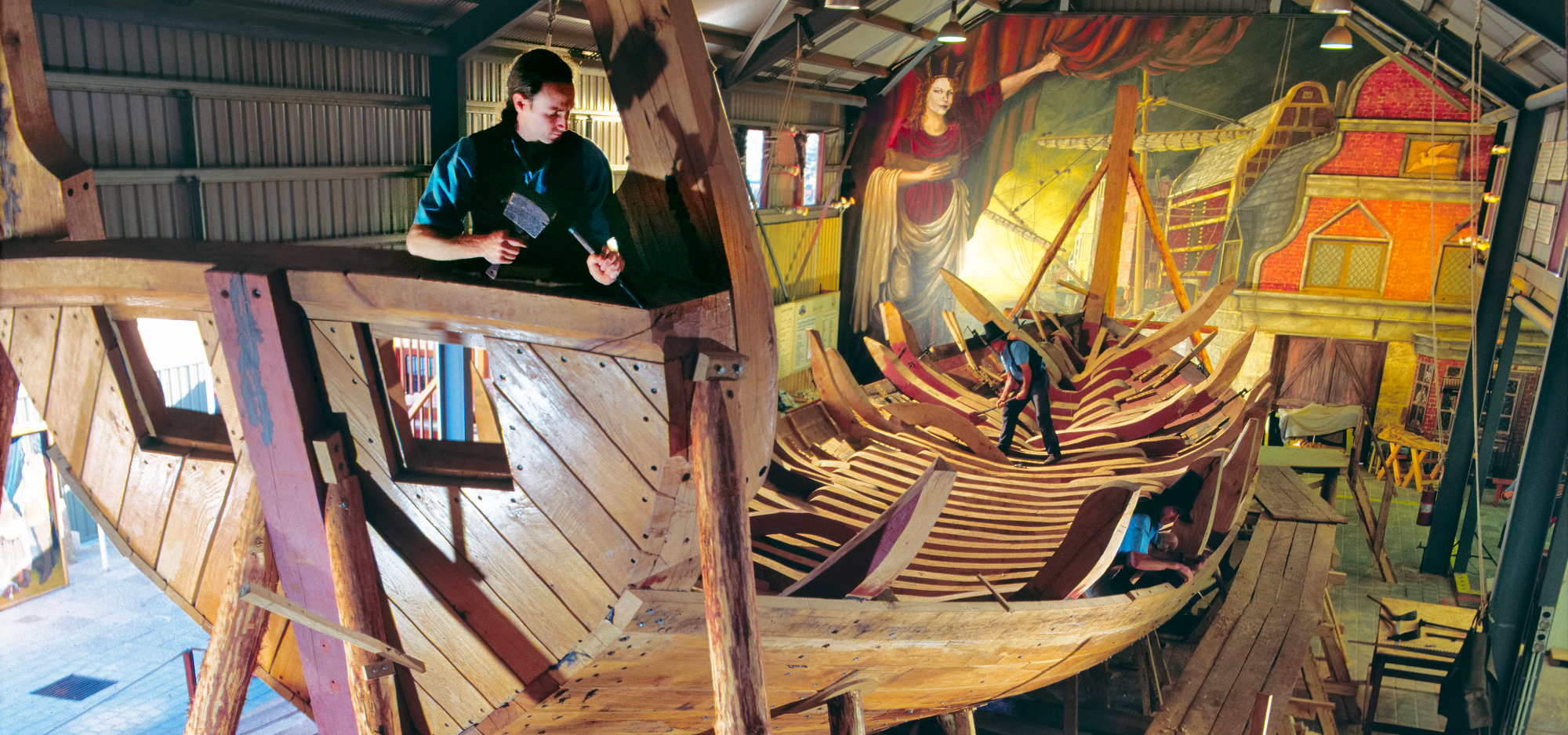 Three men using traditional hand tools to build the framework of a ship