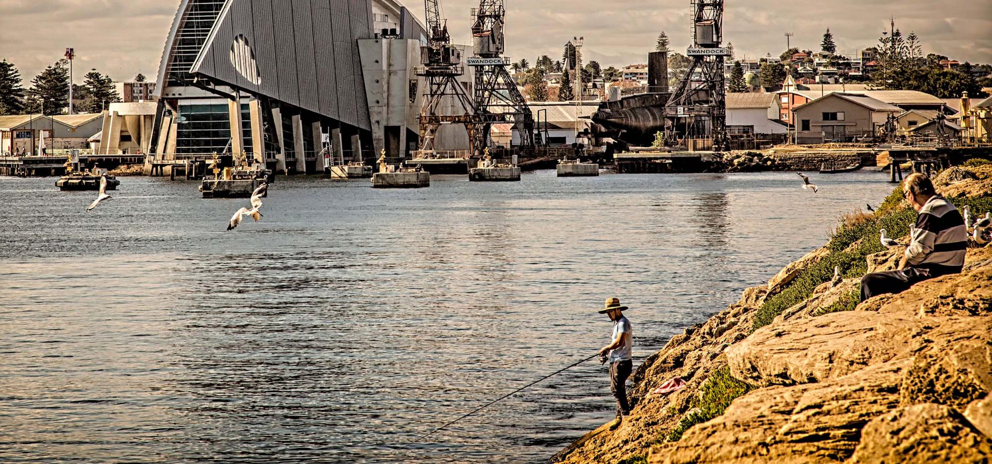 A cloudy view of Fremantle Harbour with people fishing from the rocks in the foreground