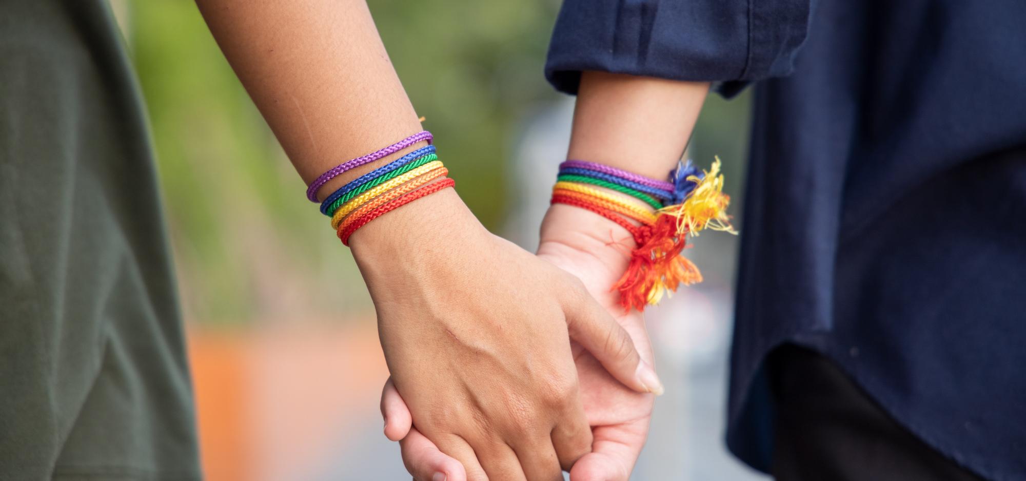 Two people holding hands with rainbow LGBTQI bracelets