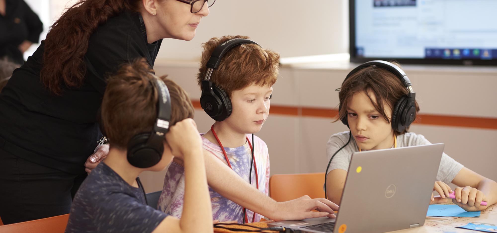A group of students around a laptop with an adult in the background