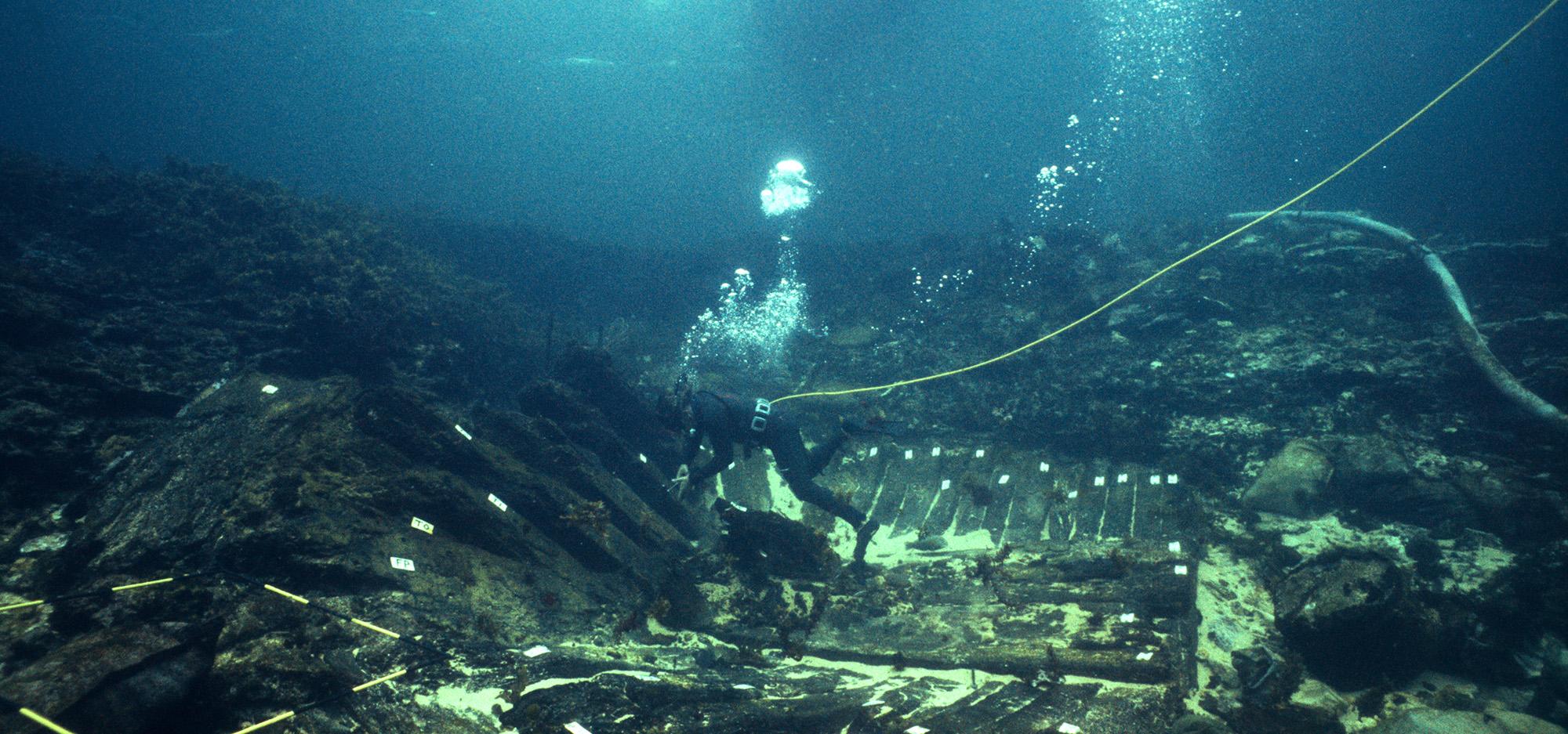 A diver swims down through deep blue water towards a sunken ship