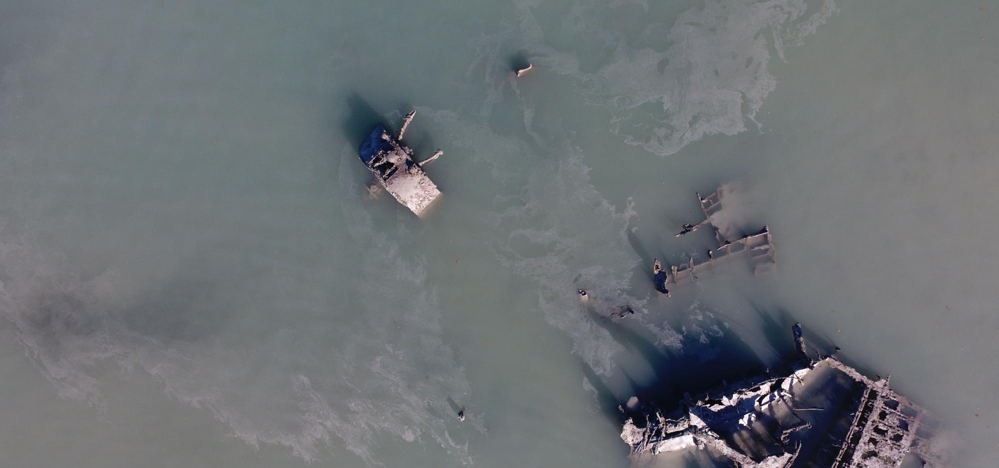 Looking down on parts of aircraft wreckage in shallow water.