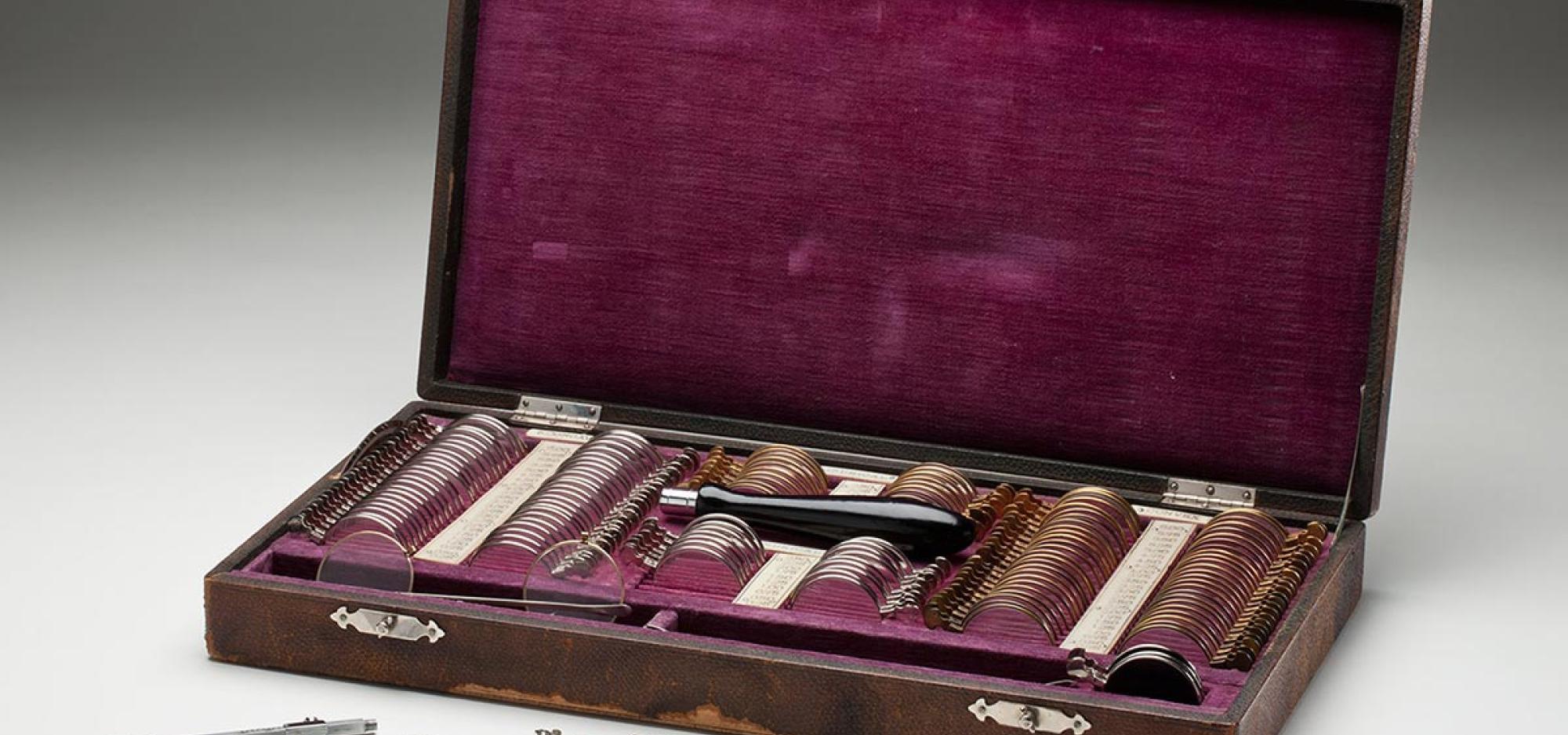 a wodden case with velvet linig. box contains slots filled with eyeglasses lenses and other instuments