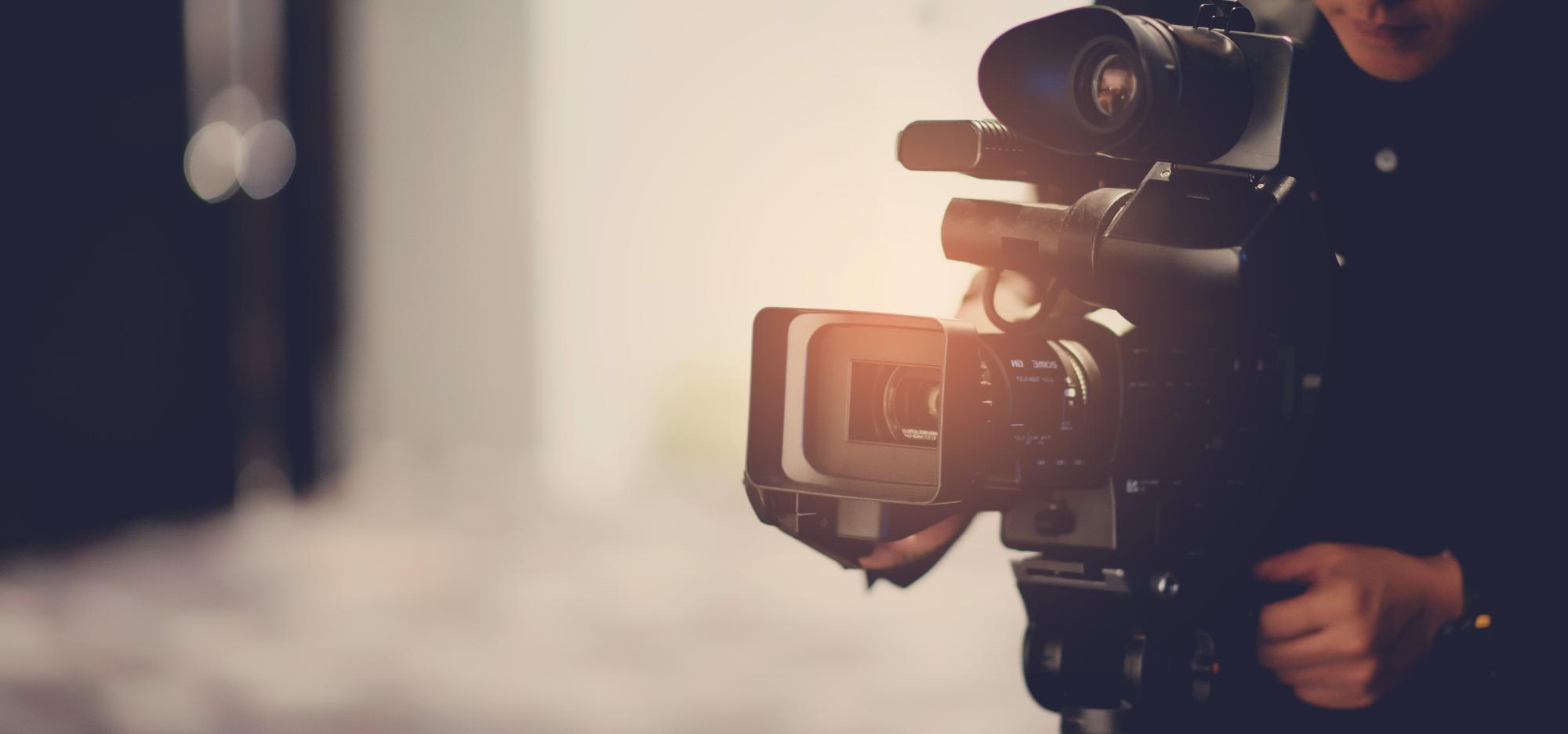 A stock image of a person operating a film camera, with their face obscured by the camera