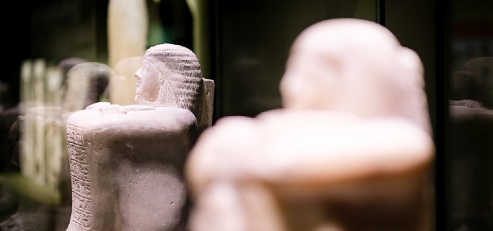 The Statue of Amenhotep-Huy depicted as a small white marble statue in the shape of a man with his knees drawn to his chest, and hieroglyphs carved into his shins. 