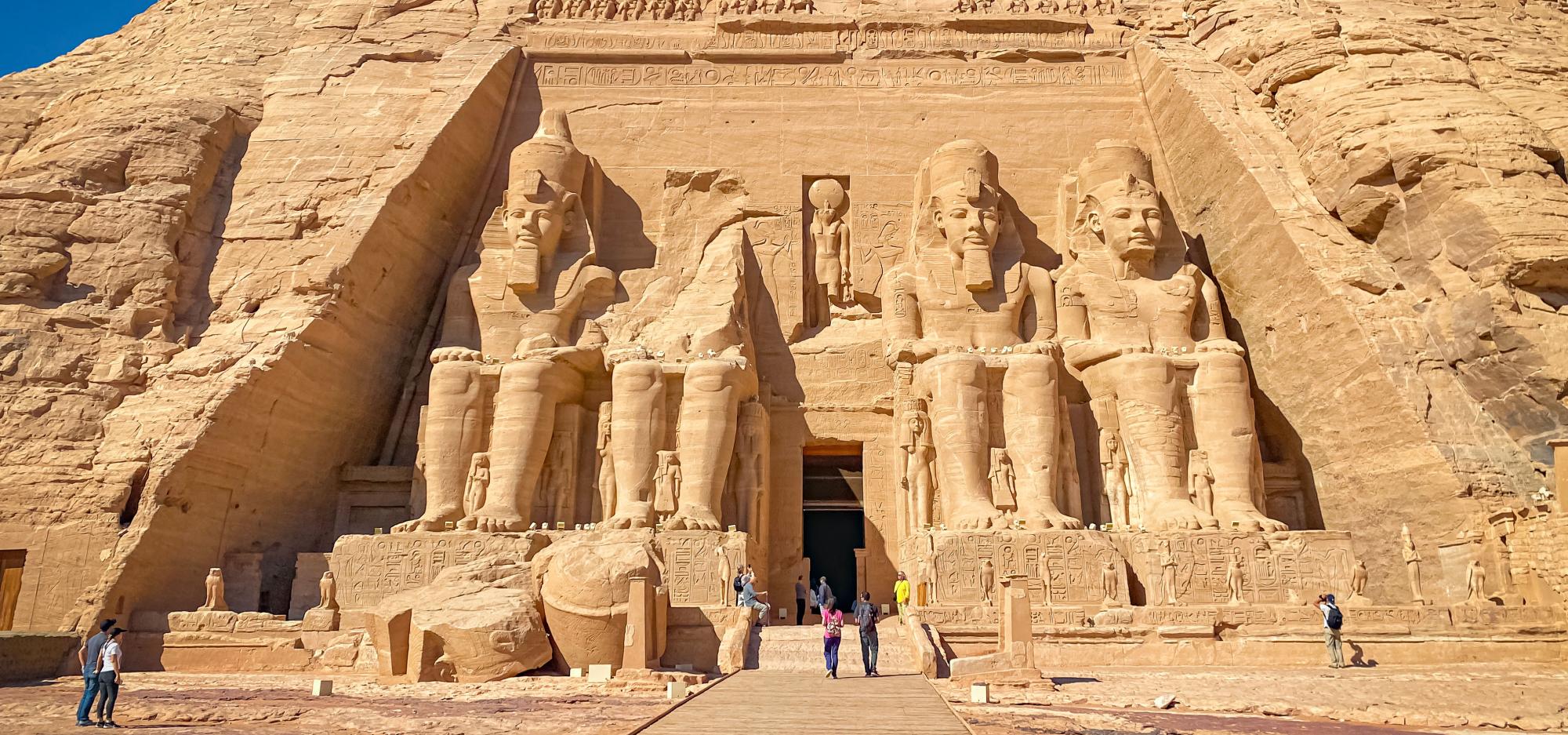 A photograph of Abu Simbel in Nubia, Egypt, where four massive statues of Ramses II sit on both sides of the entrance to a large temple cut into the site of a yellow-brown sandstone hill