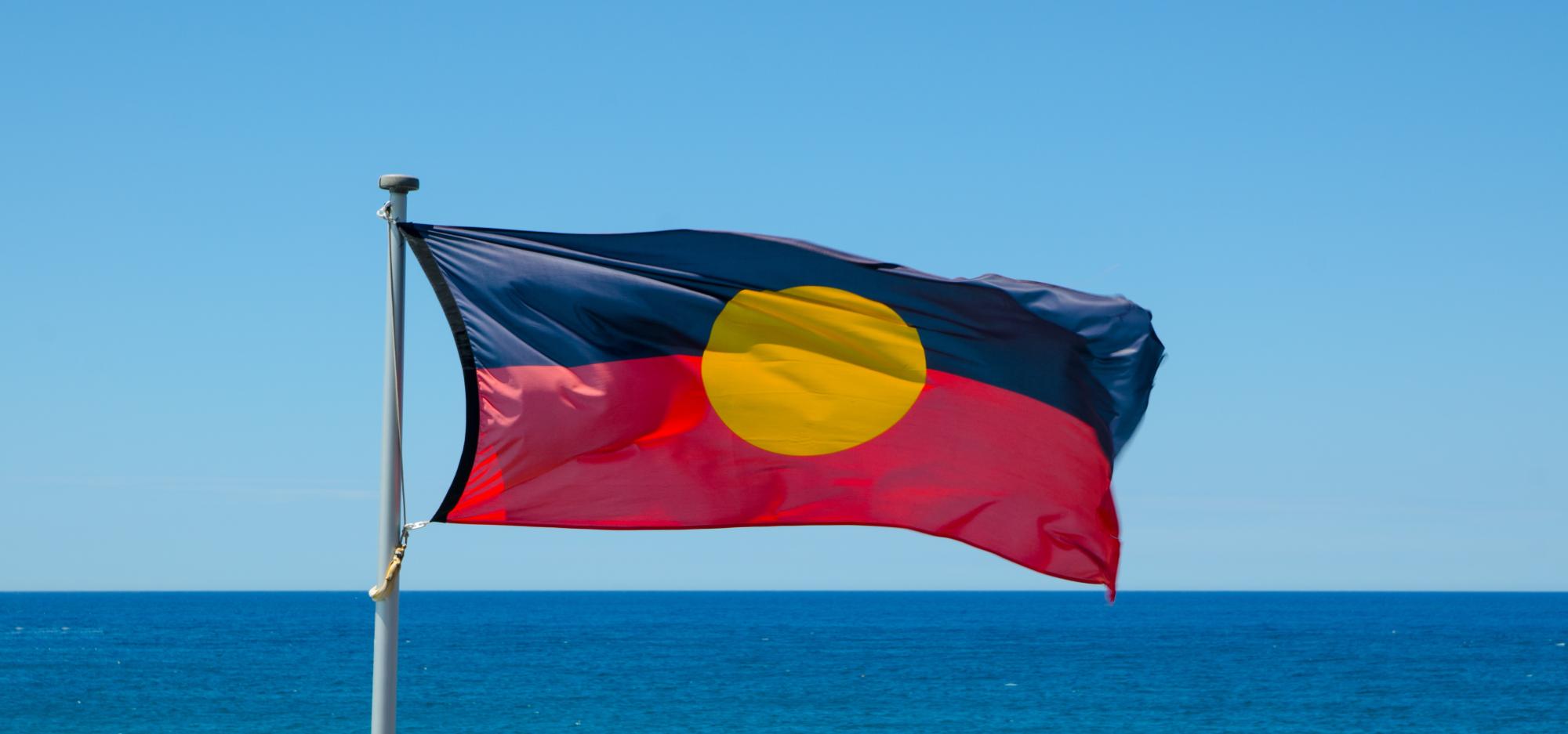The Aboriginal and Torres Strait Islander flag flies against a bright blue sky