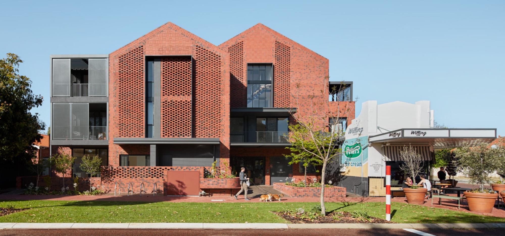 A red brick building with an industrial-style aesthetic and black steel balconies and detailing stands next to a white coffee shop on the corner with a Peters Ice Cream mural on the wall.