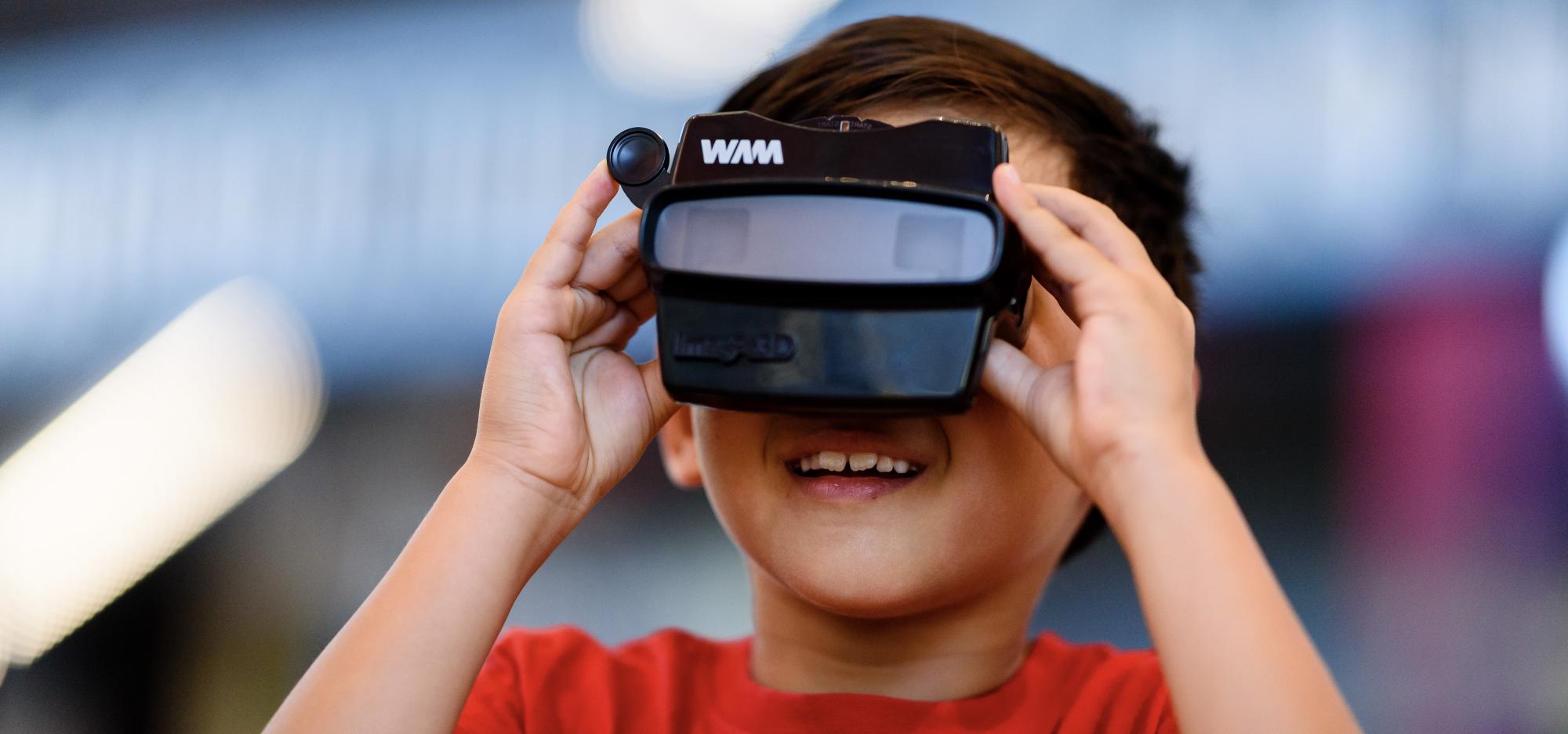 A young child holding a Viewfinder up to their face and smiling.
