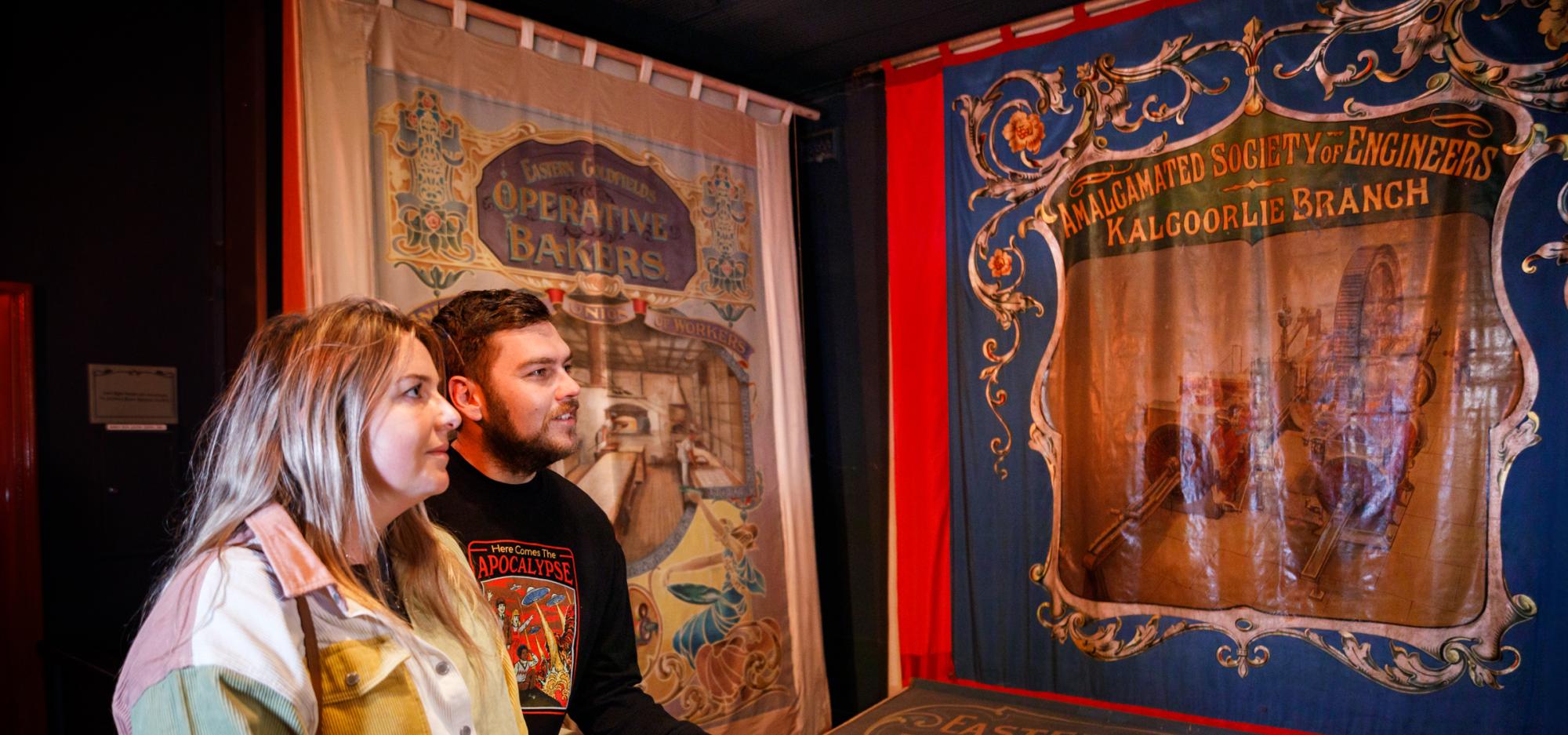 Woman and man gazing at a showcase with tapestries demonstrating Kalgoorlie's historic industries