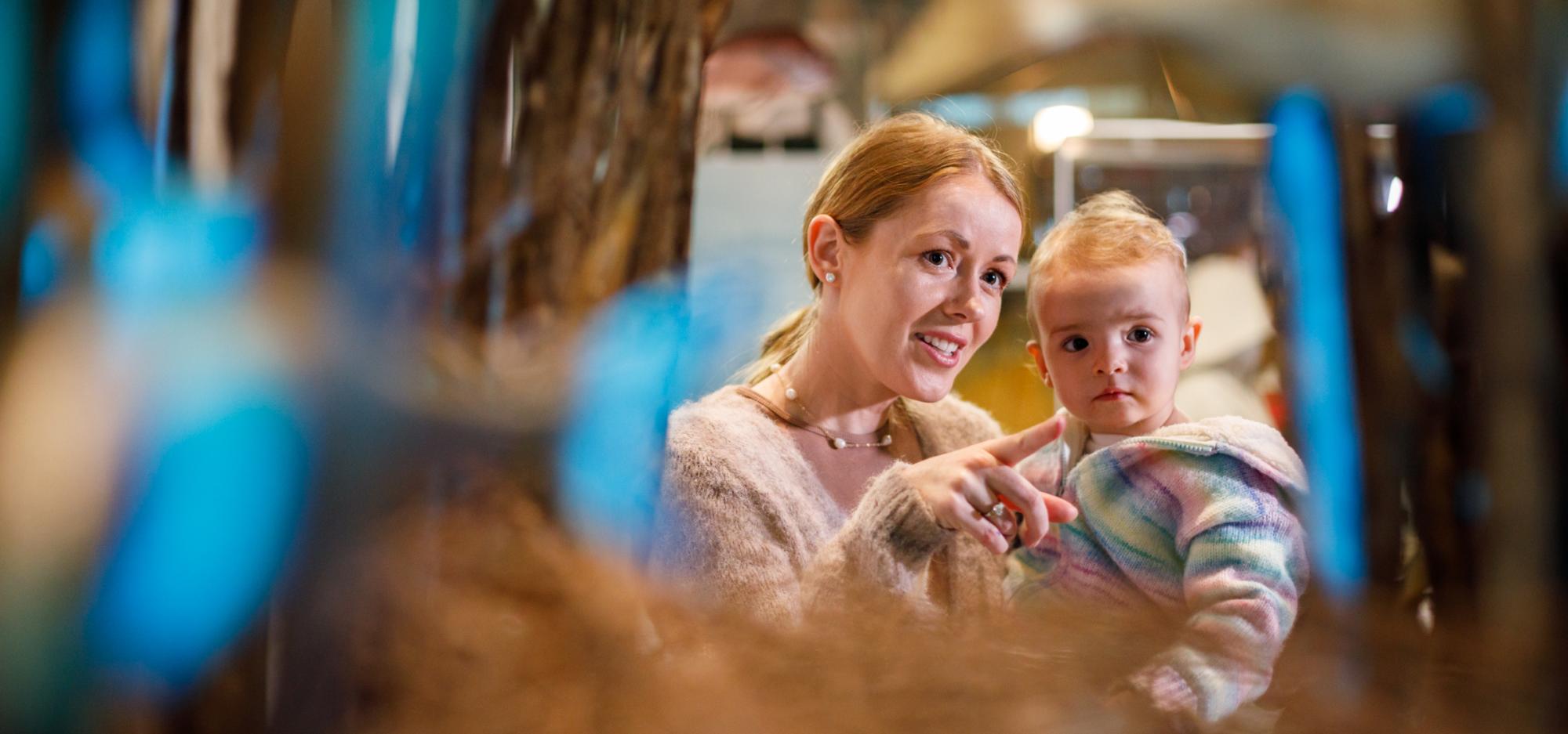 Mother holding child as they gaze through an aquarium