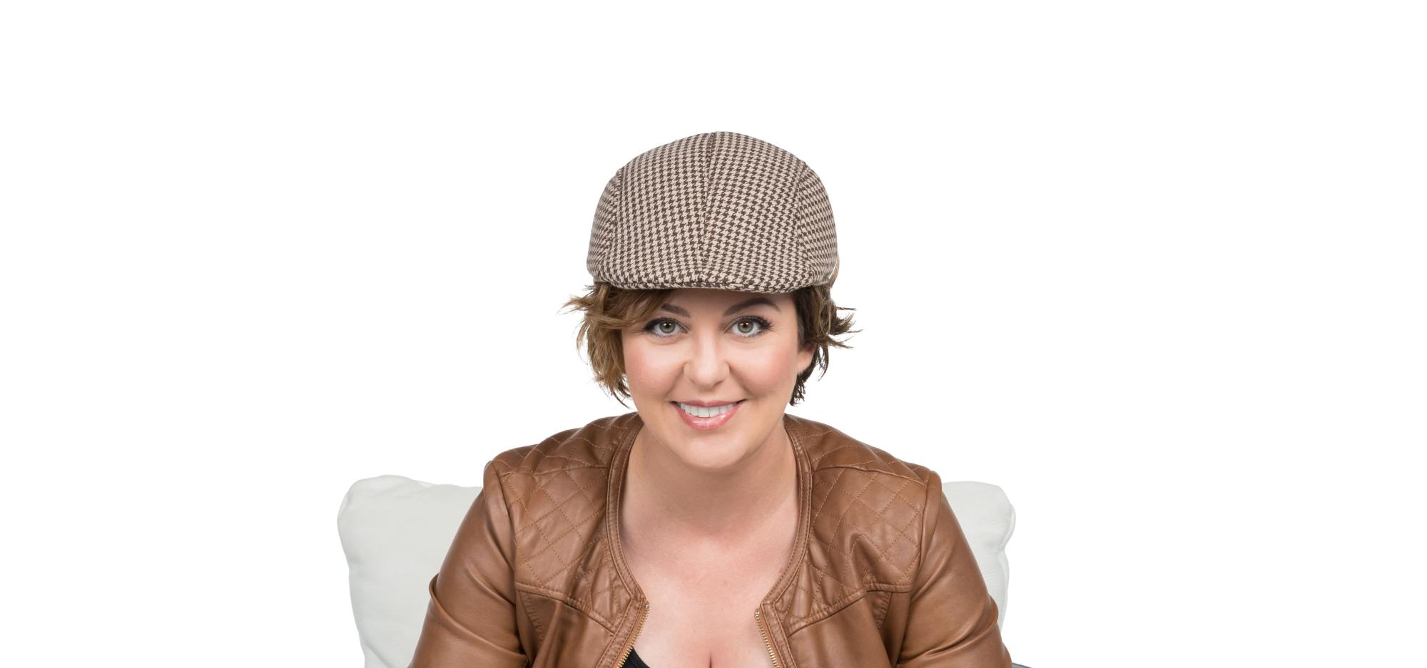 Paola is sitting in a black and white chairs facing the camera. She is smiling at the camera and wearing a Sherlock style hat while holding a pipe and magnifier glass.