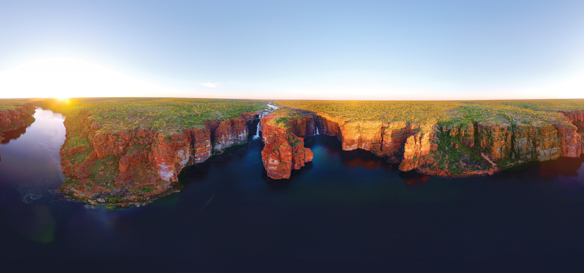 a landscape with ocean in the foreground and cliffs with waterfalls 