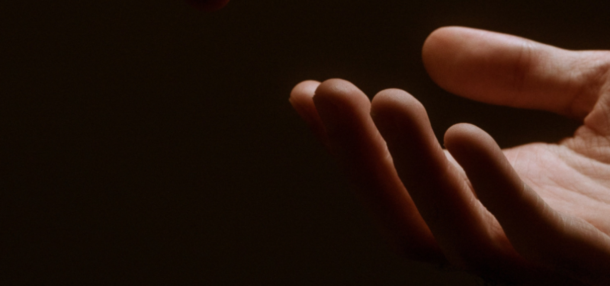 Two hands reaching towards each other against a dark background.