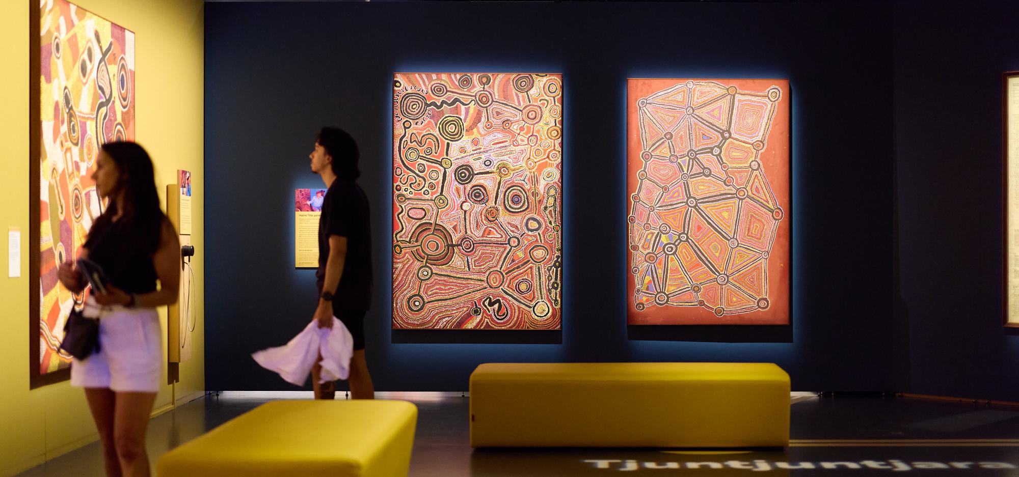 Two people in a dark gallery looking at colourful largescale painting.