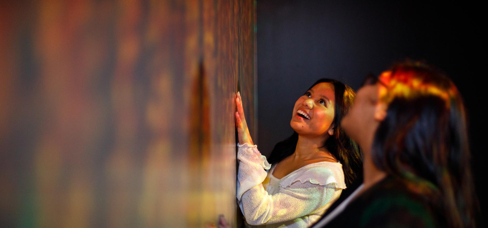 a group of adults are close to a wall of artwork and look up with a happy expression on their faces