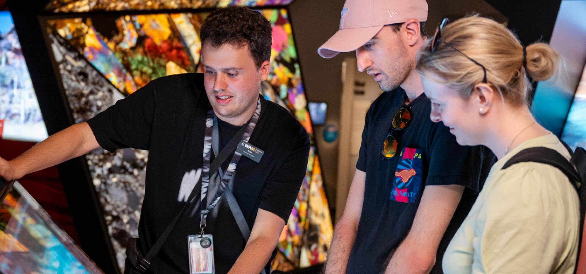 Two visitors on a tour with a staff member looking at a digital screen