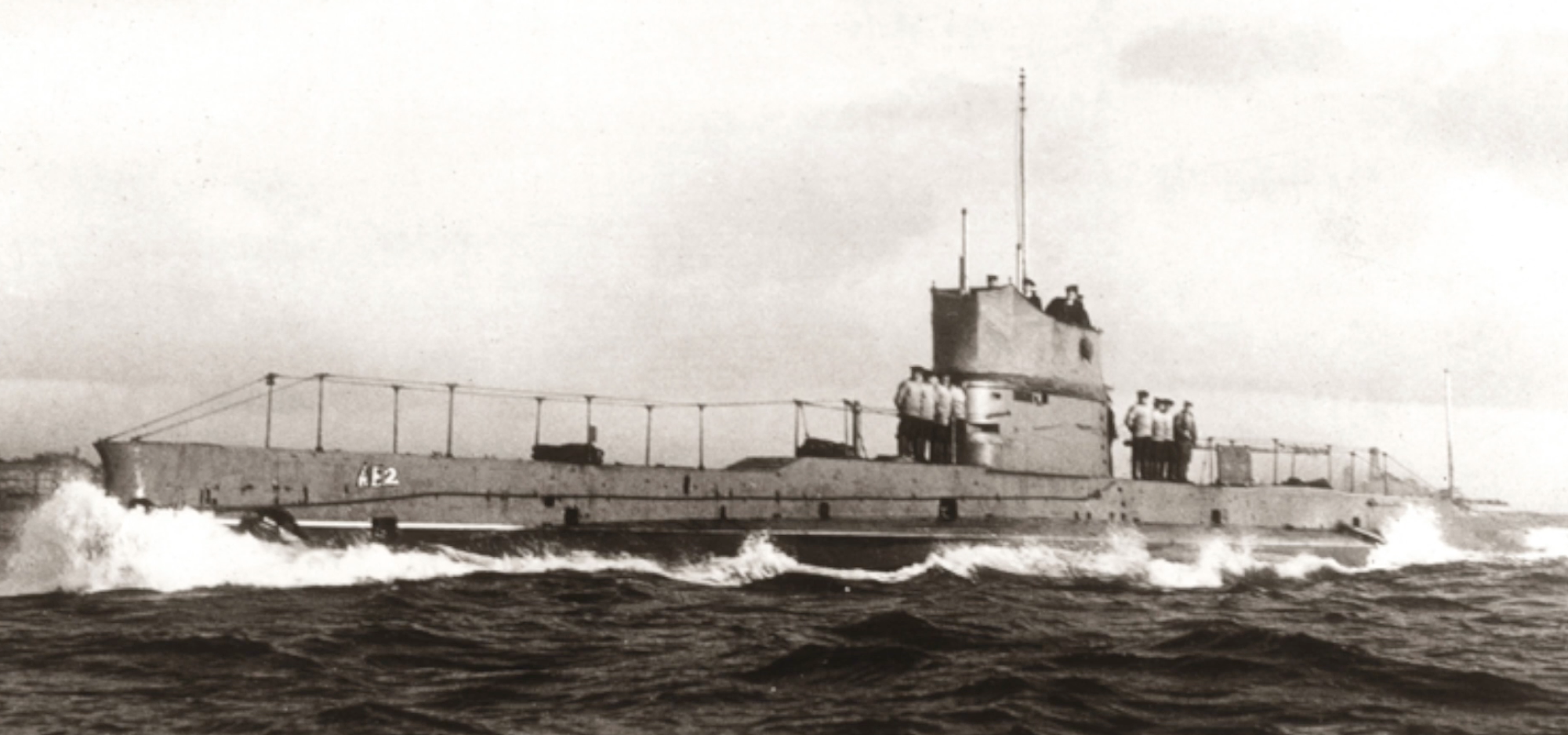 Black-and-white photo of a submarine marked “A52” travelling on rough seas, with crew standing on the deck.