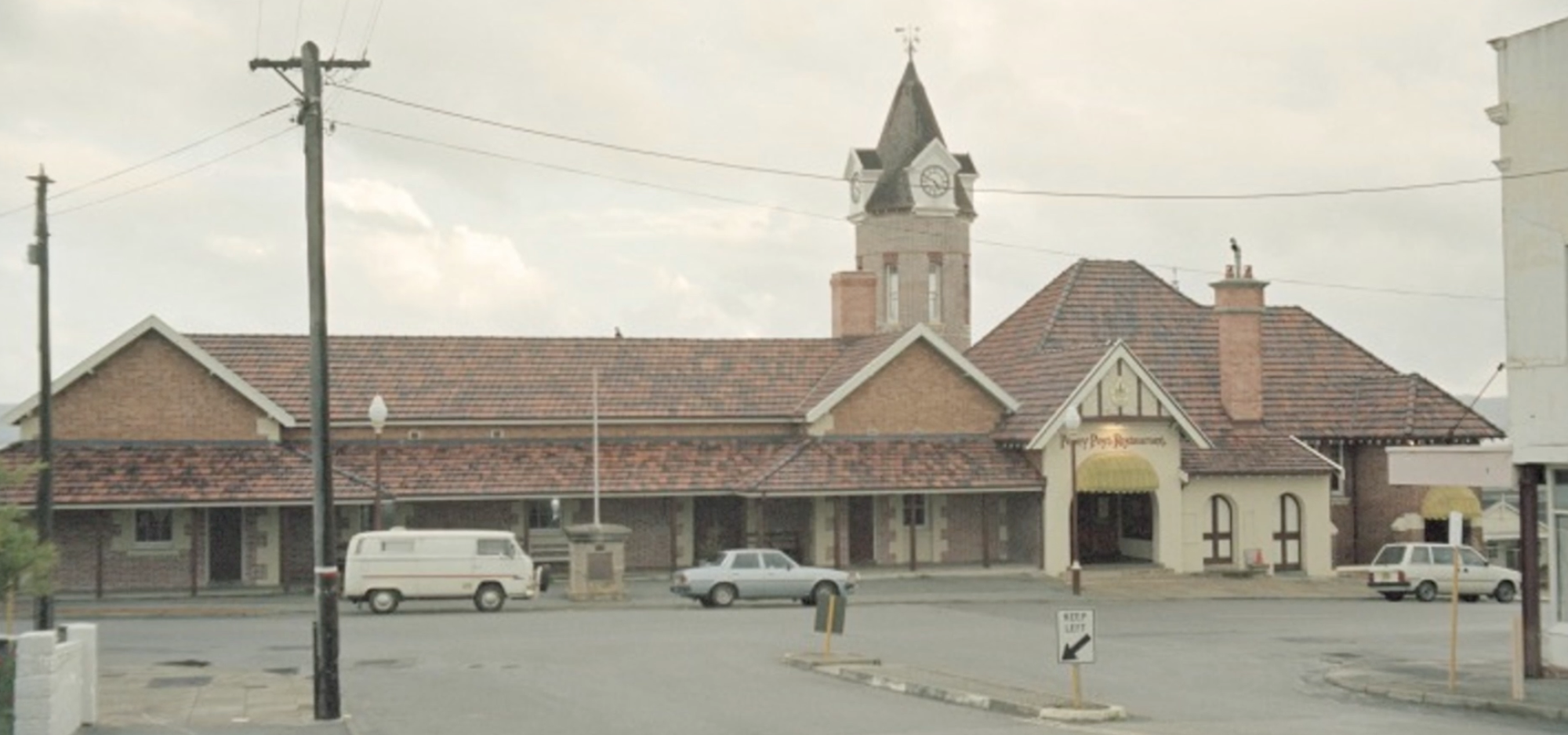 Street view of a historic railway station with a clock tower and parked cars in front.