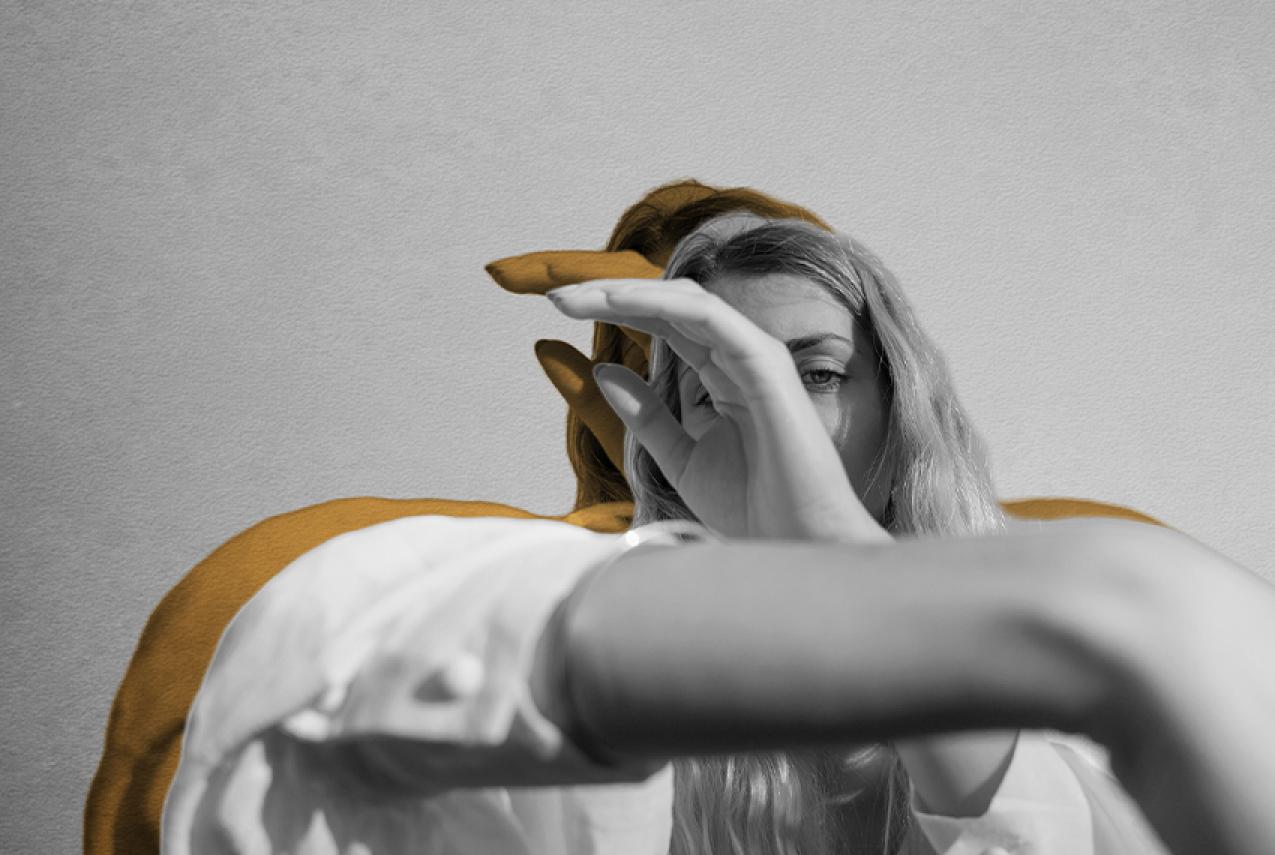 A person with long hair holding their hands in front of their face
