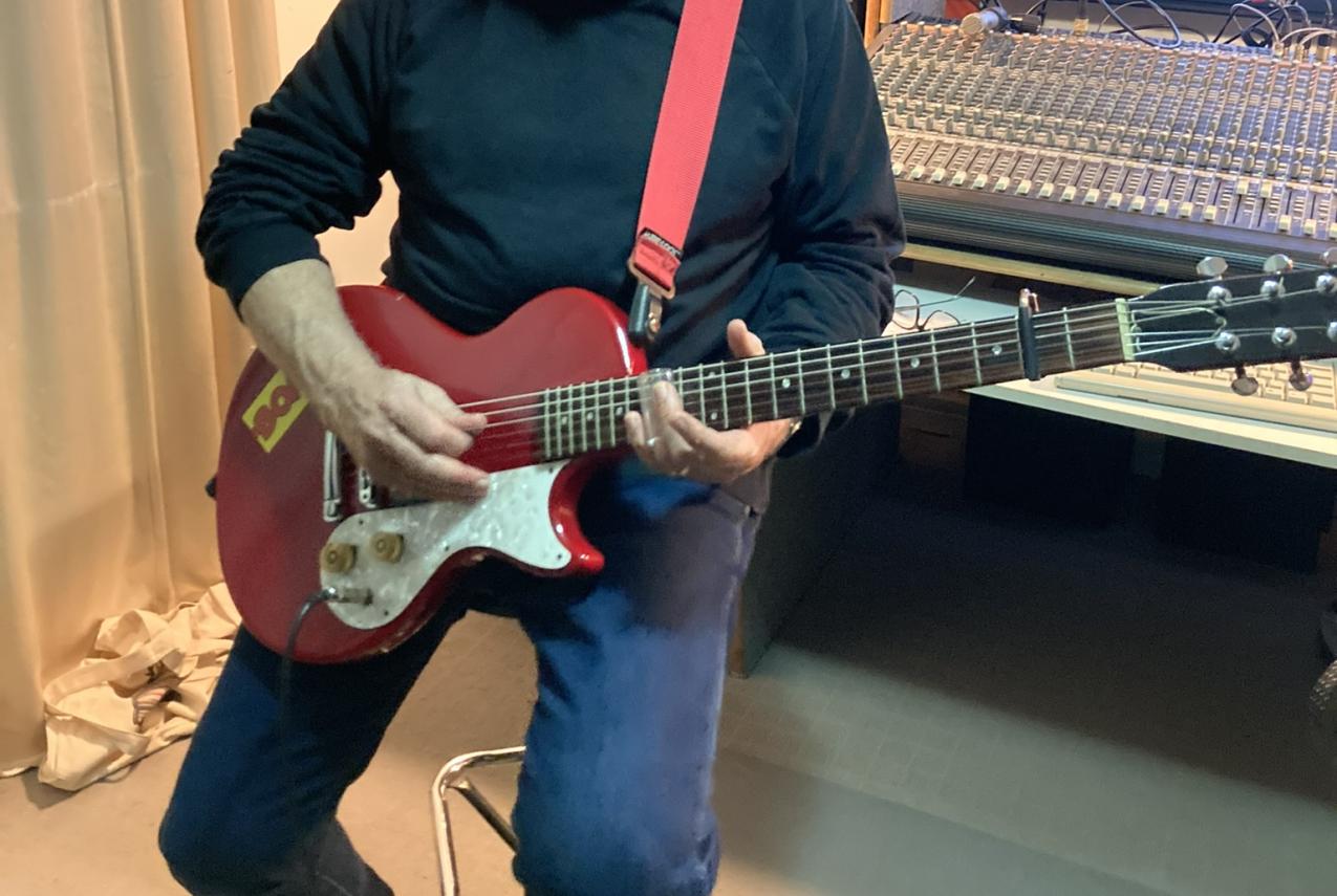 Dom Mariani strumming a guitar in his music studio.