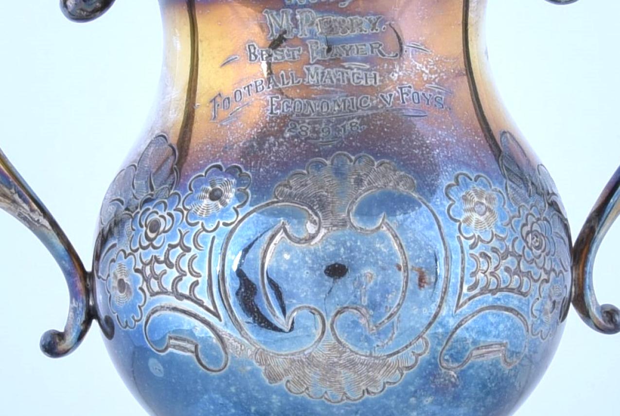 A close-up shot of the trophy engraved with 'Won by M. Perry. Best Player Football Match Economic v Foys.'